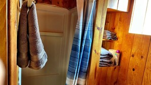 Et badeværelse med træ, badeforhæng, håndklæder og en hylde med sammenfoldede håndklæder.