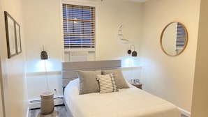 Ein ordentlich eingerichtetes Schlafzimmer mit einem Bett, Nachttischlampen, einer Uhr, einem Fenster mit Jalousien und einer Wanddekoration in Form eines Halbmondes.