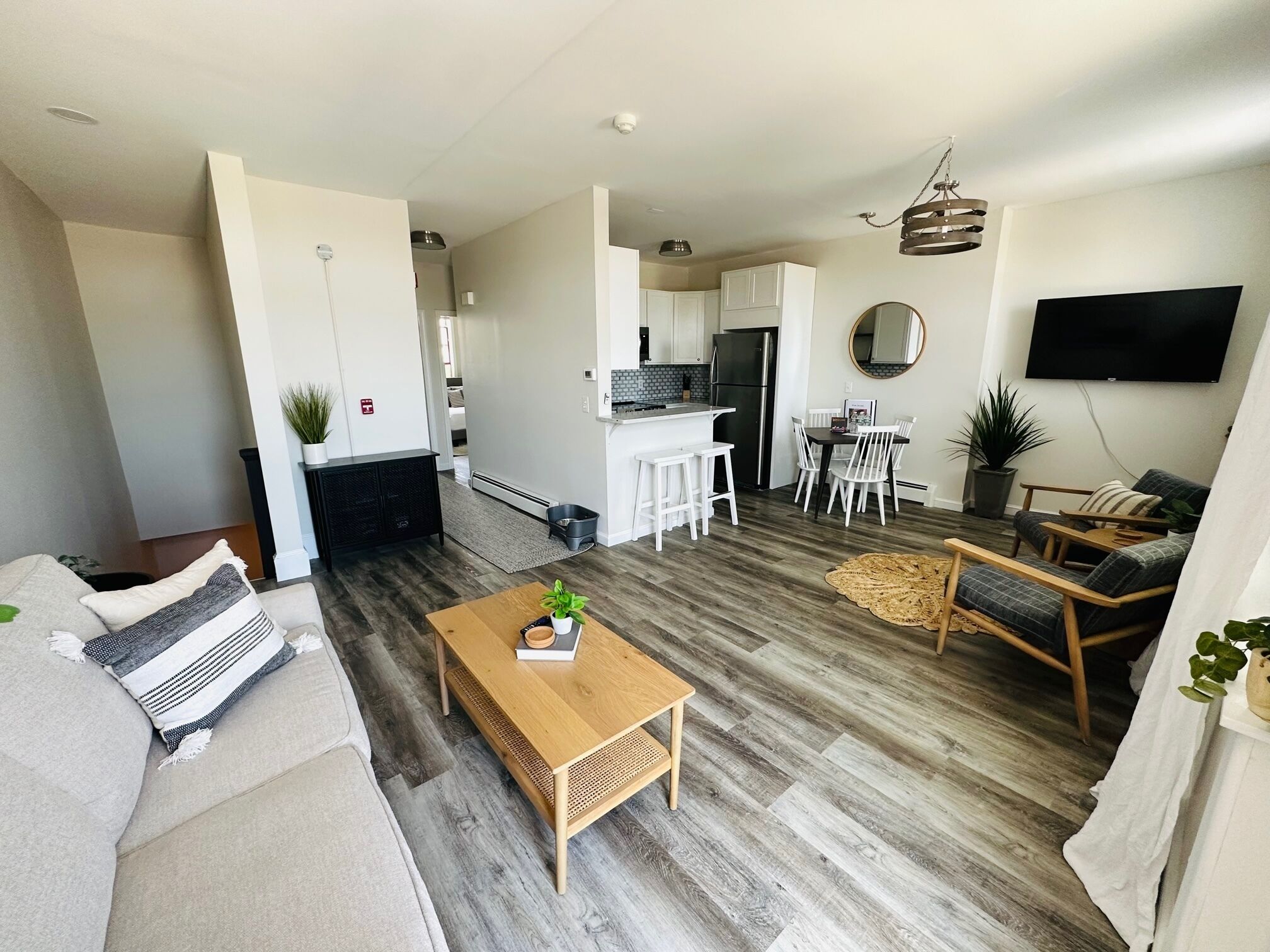 Een moderne woonkamer met een bank, een houten salontafel en een eethoek, met een keuken op de achtergrond.