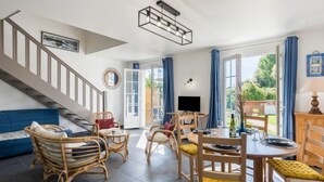 A spacious living area with a staircase, a dining table with chairs, and a television. - Bretagne by Interhome (Carnac)