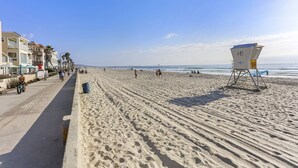 Ein Strand mit einem Rettungsturm, einem gepflasterten Weg und Badegästen.