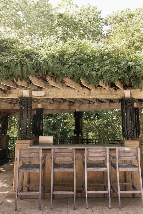 A wooden pergola with a bench seating area, surrounded by lush greenery.