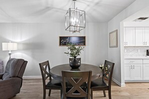 Un coin repas comprenant une table ronde, quatre chaises, un vase avec des fleurs et un luminaire suspendu.