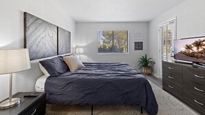 A modern bedroom with a bed, bedside table, lamp, TV, and a window with blinds. - Paradise Valley Paradise/ Ground Unit/Fresh Remodel (Phoenix)
