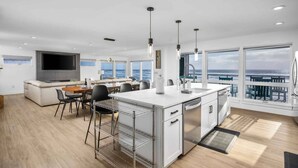 Une cuisine moderne dotée d’un grand îlot central, d’un coin repas offrant une vue agréable et d’un espace de vie avec un grand téléviseur et des sièges confortables.