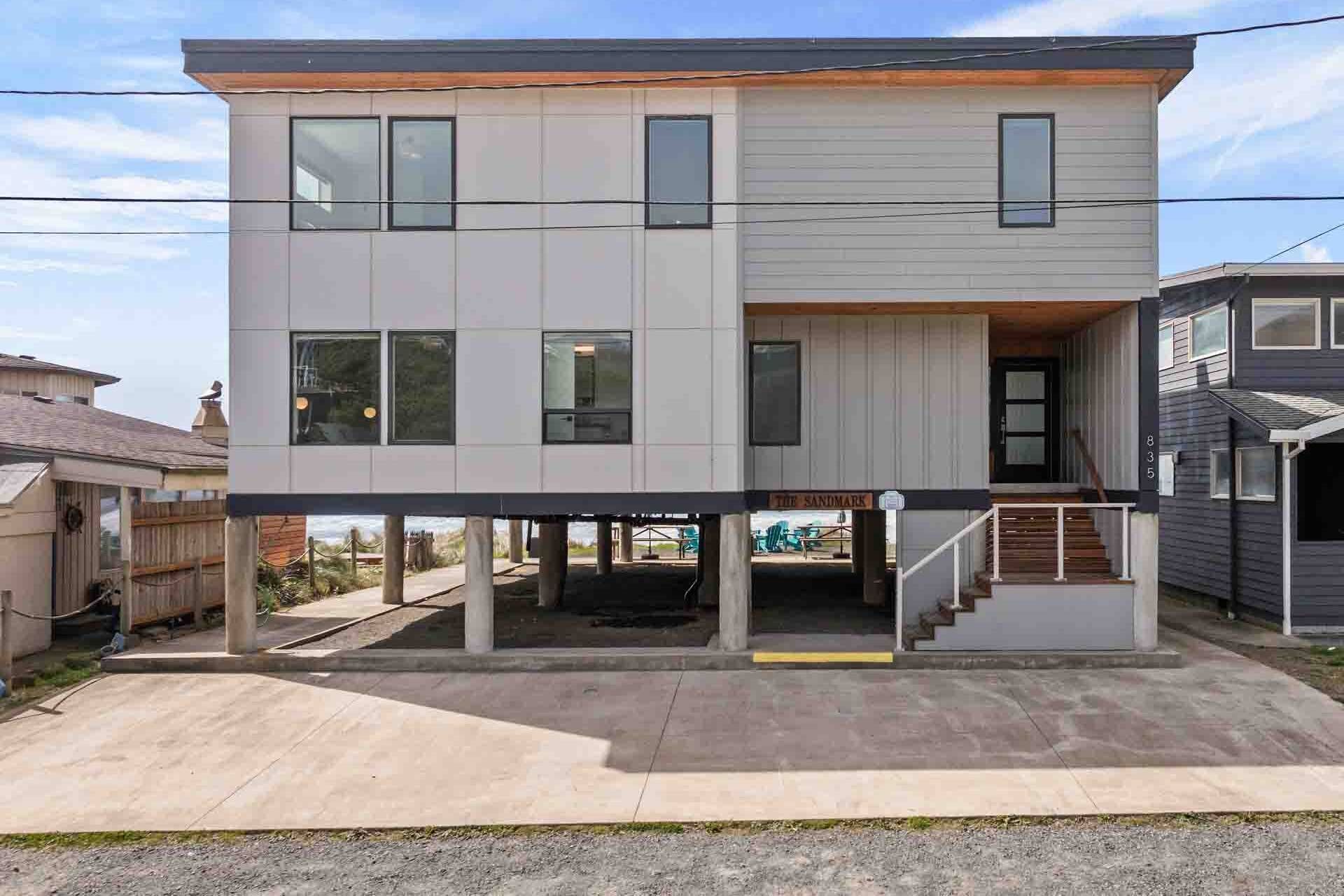 A two-story residential building with a flat roof, large windows, and a covered front porch.