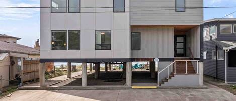 A two-story residential building with a flat roof, large windows, and a covered front porch.