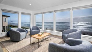 Une chambre moderne dotée de grandes fenêtres donnant sur l’océan, d’une table basse en bois et de fauteuils recouverts d’un tissu gris.
