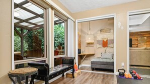 A room with a large window, a black leather bench, a grey sofa, and a small table with a woven stool. - Phenomenal Mid-Century Modern Retreat, Open Layout, Fenced Backyard, Fire-Pit, 10 Miles to Portland (Beaverton)
