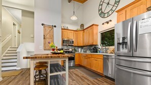 A modern kitchen with wooden cabinets, stainless steel appliances, and a central island with stools. - Phenomenal Mid-Century Modern Retreat, Open Layout, Fenced Backyard, Fire-Pit, 10 Miles to Portland (Beaverton)