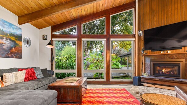A living room with a fireplace, large windows, a sofa, and a coffee table. - Phenomenal Mid-Century Modern Retreat, Open Layout, Fenced Backyard, Fire-Pit, 10 Miles to Portland (Beaverton)