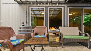 An outdoor patio with wicker furniture, a wooden table, and a fire feature. - Phenomenal Mid-Century Modern Retreat, Open Layout, Fenced Backyard, Fire-Pit, 10 Miles to Portland (Beaverton)