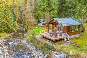 A cabin with a deck, a small porch, and a view of a stream. - Rivers Edge Retreat - Near Snoqualmie Pass Ski Area (Issaquah)