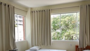 Une pièce avec trois lits, une chaise en bois et une fenêtre avec des rideaux.