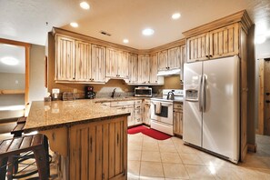 A kitchen with wooden cabinets, a granite countertop, a stainless steel refrigerator, and a red rug. - Top Floor Prospector Condo - 3BD/3BA - Sleep up to 10 (Park City)