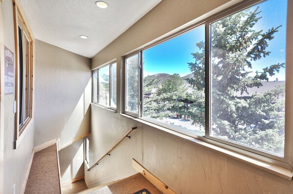 Una habitación con amplios ventanales, una escalera de madera y vistas a árboles y colinas.