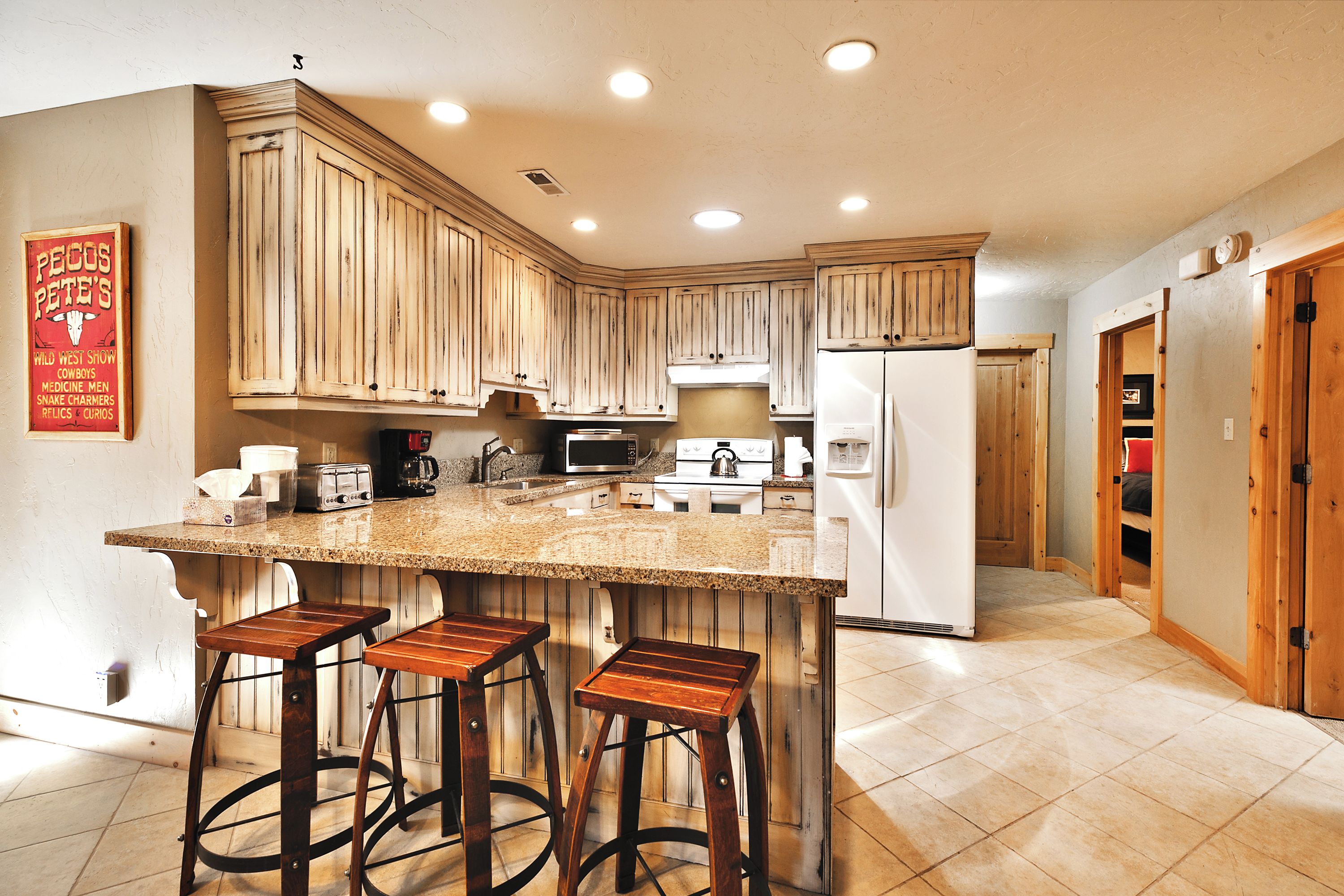 A kitchen with wooden cabinets, a granite countertop, a refrigerator, a stove, and bar stools.