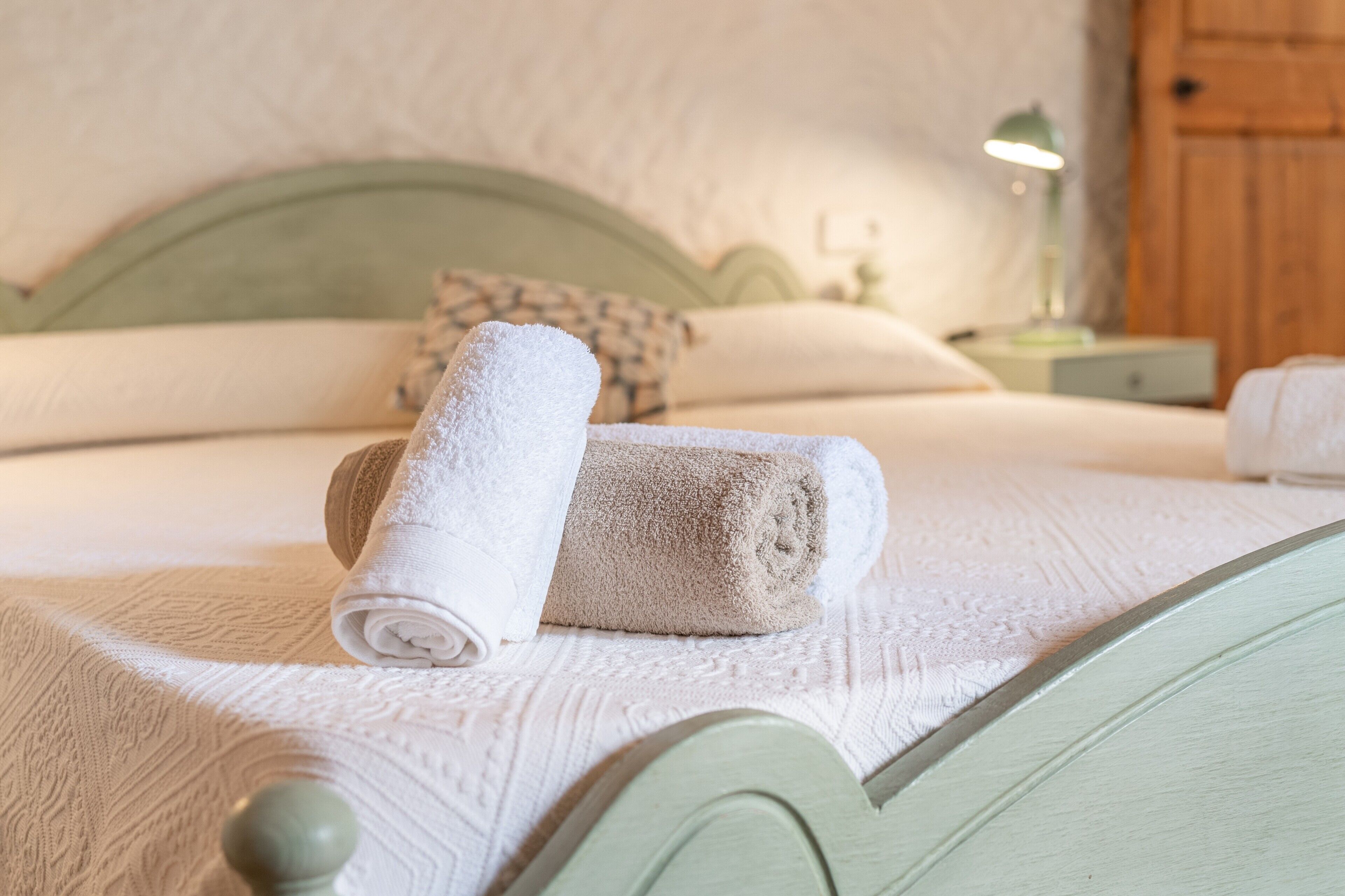 A neatly made bed with a green headboard, a white textured bedspread, and a pair of folded towels.