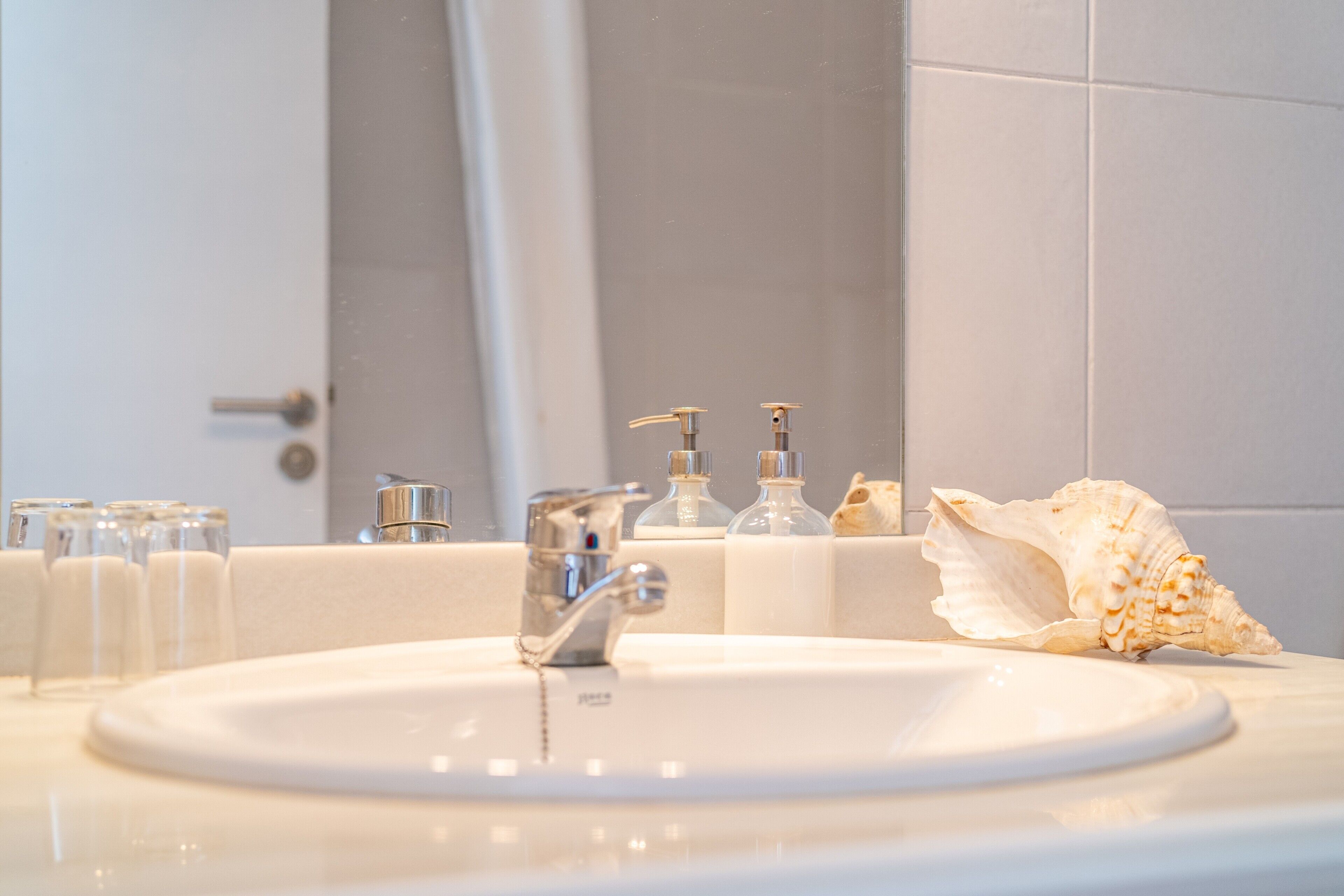 A bathroom sink with a faucet, a large seashell, and several glass bottles.