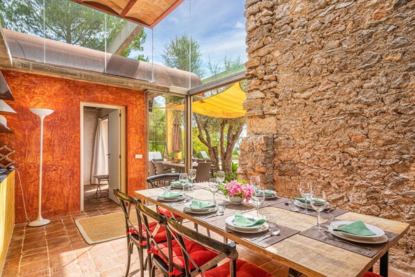 An outdoor dining area with a stone wall, a wooden table set for four, and red cushioned chairs.