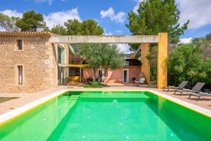 A swimming pool with a stone building, a glass structure, and outdoor seating.