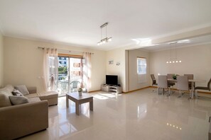 A modern living room with a sofa, a coffee table, a TV, and a dining area with chairs and a table.