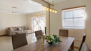 A modern living room with a dining table, sofa, and a large window. - Apartamento Água Brisa with Pool, Wi-Fi, A/C, Balcony & Garden (Albufeira)