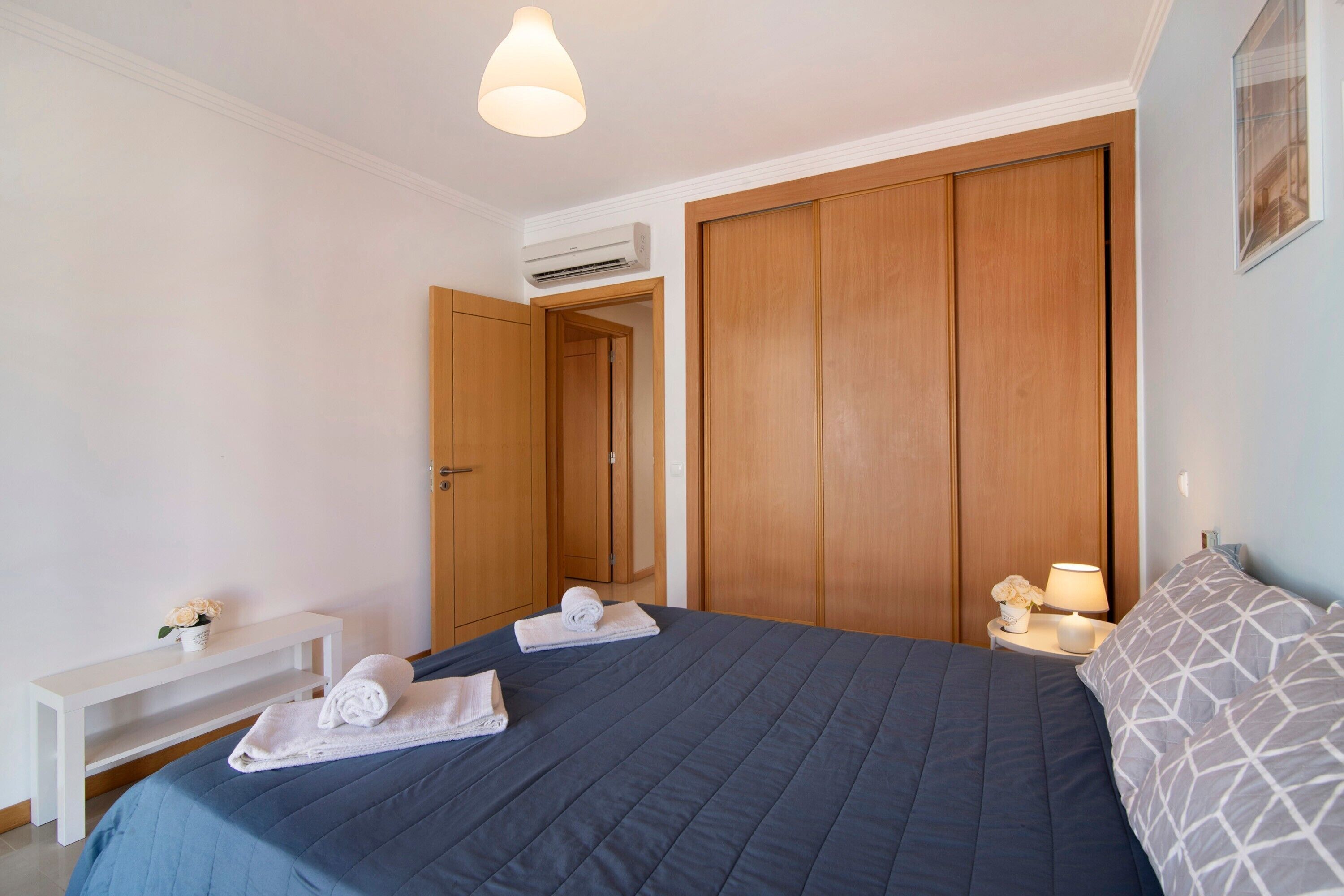 Una habitación de hotel con una cama, una mesita de noche con lámpara, un banco y un armario.