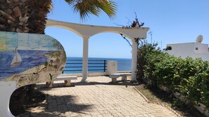 A paved patio with a mural, a white column structure, and a view of the sea. - Apartamento Água Brisa with Pool, Wi-Fi, A/C, Balcony & Garden (Albufeira)