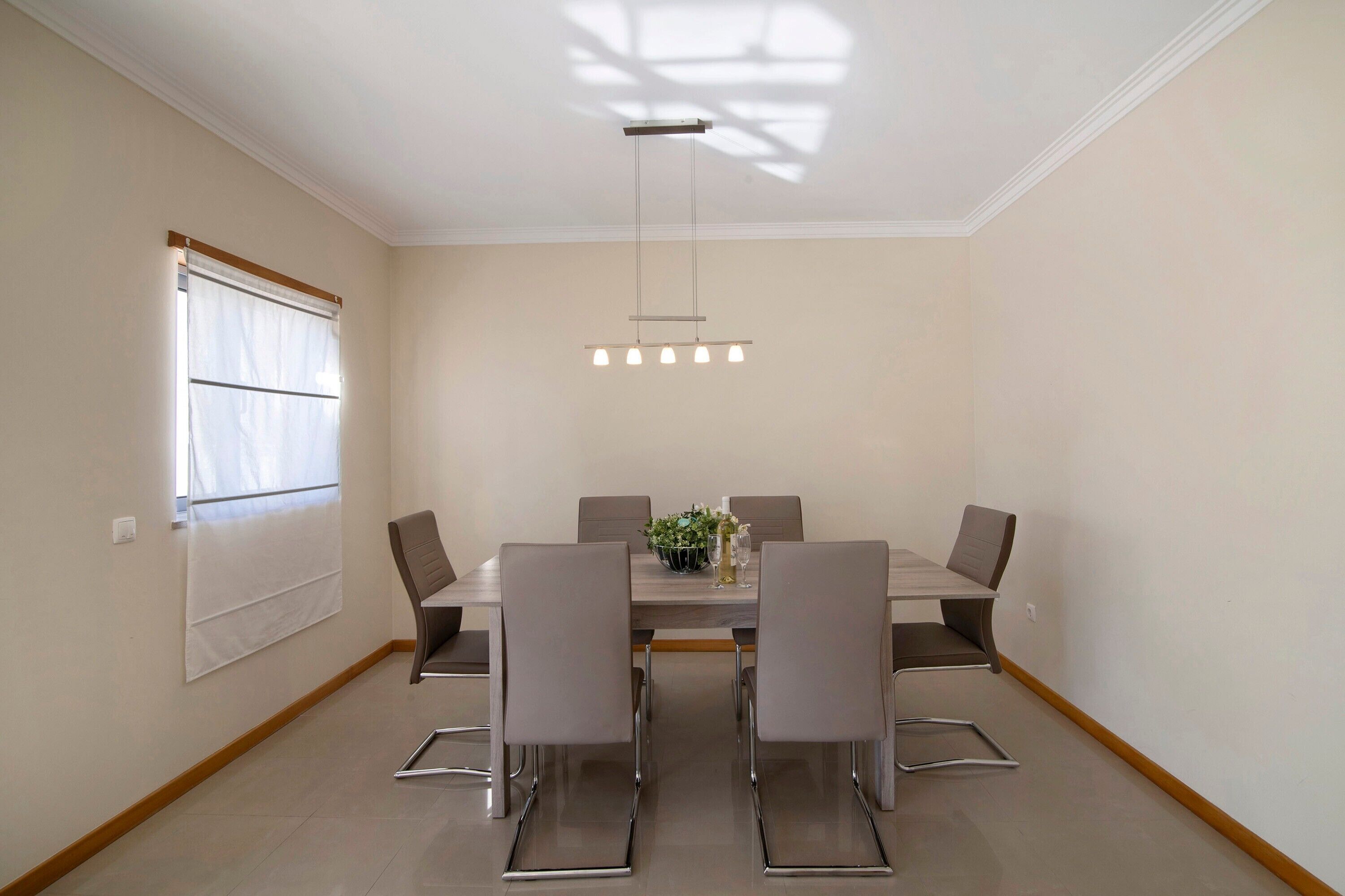 A dining area with a table, chairs, a hanging light fixture, and a window with blinds.