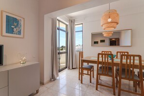 Un espace repas comprenant une table, des chaises, un luminaire suspendu et une grande fenêtre avec des rideaux.