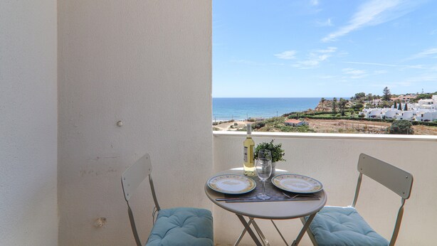 A balcony with a table set for two, overlooking a coastal view.