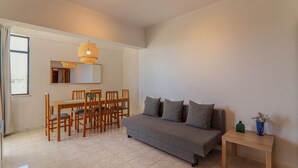 A living room with a sofa, dining table, chairs, and a hanging light fixture.