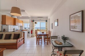 A modern kitchen with wooden cabinets, a dining area with a glass table, and a sofa.