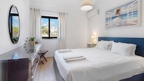 Une chambre d’hôtel comprenant un lit, un bureau, une chaise, un miroir, une fenêtre avec des rideaux, une lampe fixée au mur et un tableau.