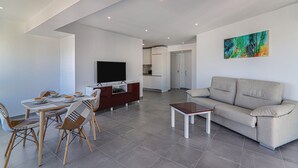 Ein modernes Wohnzimmer mit Sofa, Fernseher, Esstisch und Stühlen.
