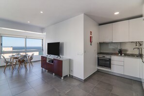 A modern kitchen with a TV, dining area with chairs, and a view of the sea.
