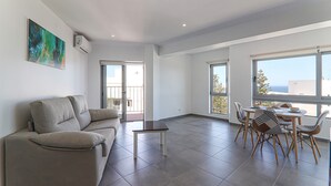 Ein modernes Wohnzimmer mit einer Couch, einem Esstisch mit Stühlen und großen Fenstern mit Blick.