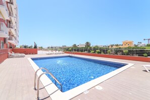Piscina no terraço com águas cristalinas azuis, espreguiçadeiras e vista para a paisagem urbana.
