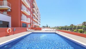 A swimming pool with clear blue water, surrounded by a red building with balconies and a lifebuoy on the edge. - Quinta dos Arcos Lote 18 3ºG Apartment with Sea View, Pool and Balcony (Armação de Pêra)