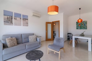 Un salon moderne avec un canapé gris, une petite table ronde et un coin repas comprenant une table et des chaises blanches.