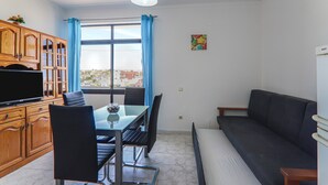 A room with a dining table, chairs, a sofa, a TV, and a window with curtains. - Torre Sol 909 Beach Apartment with Pool, Garden, and Balcony (Armação de Pêra)