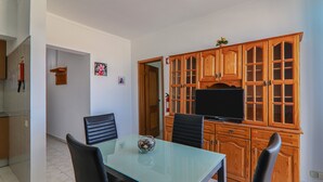 A dining area with a glass table, black chairs, wooden cabinets, and a television. - Torre Sol 909 Beach Apartment with Pool, Garden, and Balcony (Armação de Pêra)