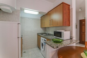 A compact kitchen with a washing machine, microwave, and granite countertop.
