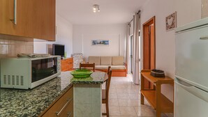 Eine kleine Küche mit Mikrowelle, einer grünen Schüssel, einem Holzschrank und einem weißen Kühlschrank.