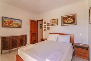 A bedroom with a bed, wooden nightstand, dresser, and wall-mounted artwork.