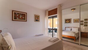 Een slaapkamer met een bed, een spiegel in de badkamer en een balkon met stoelen.