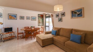 Een woonkamer met een bank, een eettafel met stoelen, een tv op een dressoir en diverse ingelijste foto's aan de wand.