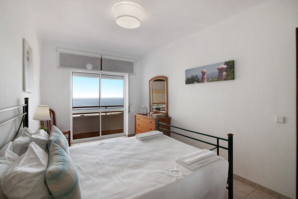 A bedroom with a bed, a dresser, a mirror, and a window with a view.