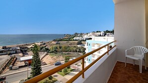 A balcony with a white plastic chair, a railing, and a view of the sea and buildings.